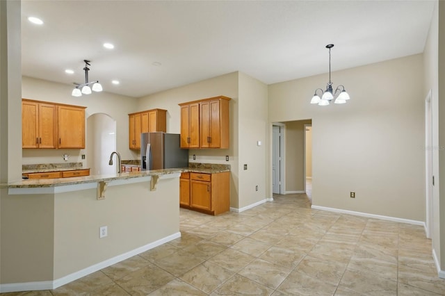 5340 Riva Ridge Dr, Wesley Chapel, FL 33544 - kitchen featuring stainless steel fridge, a chandelier, light stone countertops, a breakfast bar, and arched walkways