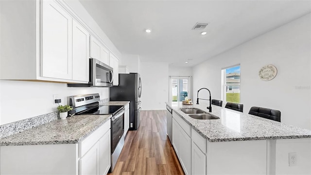 35552 Shade Fern Ln, Zephyrhills, FL 33541 - kitchen with appliances with stainless steel finishes, a sink, wood finished floors, an island with sink, and white cabinetry