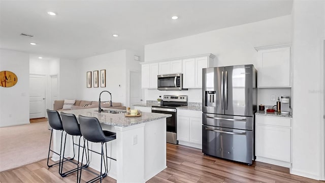 35552 Shade Fern Ln, Zephyrhills, FL 33541 - kitchen featuring appliances with stainless steel finishes, a sink, white cabinets, wood finished floors, and a kitchen island with sink