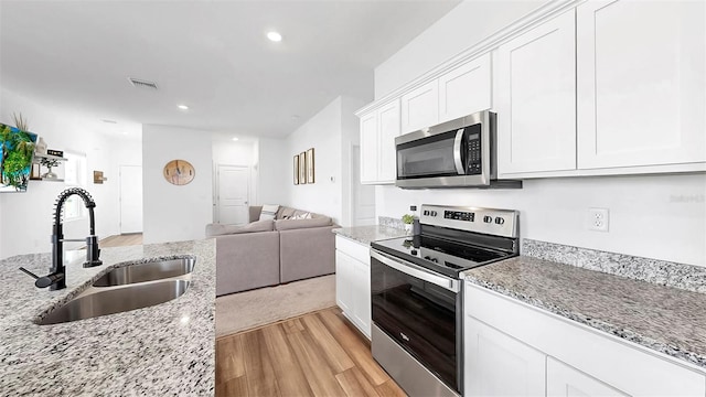 35552 Shade Fern Ln, Zephyrhills, FL 33541 - kitchen with stainless steel appliances, a sink, light wood-style flooring, open floor plan, and white cabinets