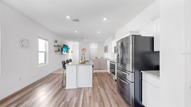 35552 Shade Fern Ln, Zephyrhills, FL 33541 - kitchen featuring stainless steel appliances, white cabinetry, light wood-style flooring, an island with sink, and a kitchen breakfast bar