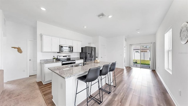 35552 Shade Fern Ln, Zephyrhills, FL 33541 - kitchen with appliances with stainless steel finishes, a center island with sink, a breakfast bar, white cabinetry, and wood finished floors