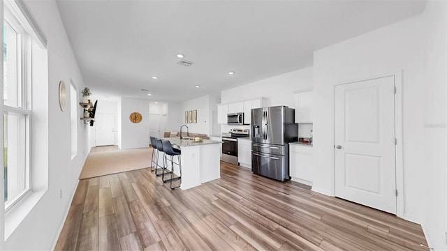 35552 Shade Fern Ln, Zephyrhills, FL 33541 - kitchen featuring stainless steel appliances, light wood-style flooring, a breakfast bar area, white cabinets, and recessed lighting
