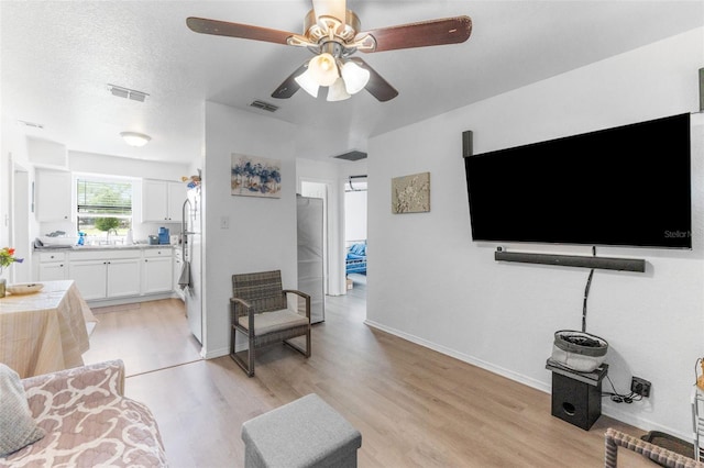 living room featuring light wood finished floors, a ceiling fan, and baseboards