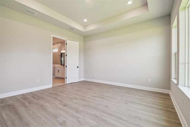 spare room featuring light wood finished floors, a raised ceiling, baseboards, and recessed lighting