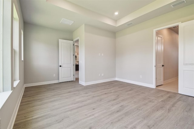 empty room featuring light wood finished floors, baseboards, recessed lighting, and a tray ceiling