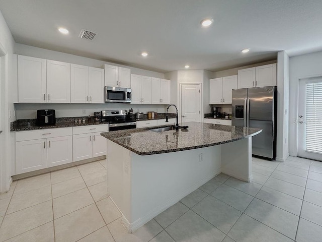 6444 Bar S Bar Trl, Zephyrhills, FL 33541 - kitchen featuring stainless steel appliances, a sink, white cabinets, dark stone counters, and an island with sink