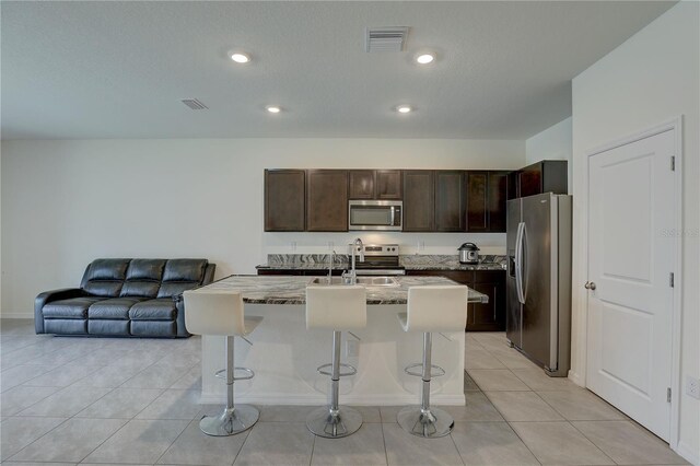 33062 Frosted Clover Way, Wesley Chapel, FL 33545 - kitchen featuring appliances with stainless steel finishes, a kitchen breakfast bar, a sink, dark brown cabinetry, and light stone counters