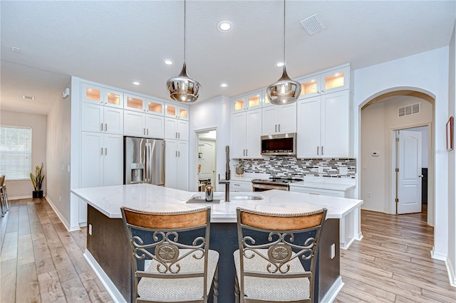 445 Arch Ridge Loop, Seffner, FL 33584 - kitchen with stainless steel appliances, arched walkways, decorative backsplash, light wood-type flooring, and a kitchen island with sink