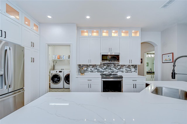 445 Arch Ridge Loop, Seffner, FL 33584 - kitchen with stainless steel appliances, washer and clothes dryer, a sink, arched walkways, and white cabinets