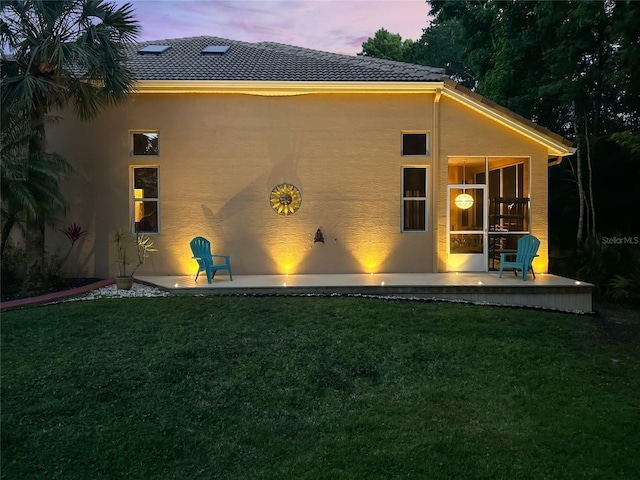 7246 Gaberia Rd, New Port Richey, FL 34655 - back of property at dusk featuring stucco siding, a yard, and a patio
