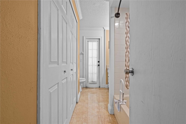 hallway with crown molding, light tile patterned flooring, and a textured ceiling