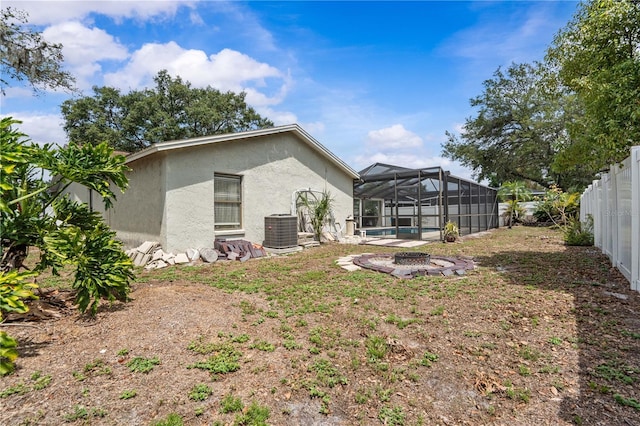 rear view of house with stucco siding, central AC, a swimming pool, a fenced backyard, and a lanai