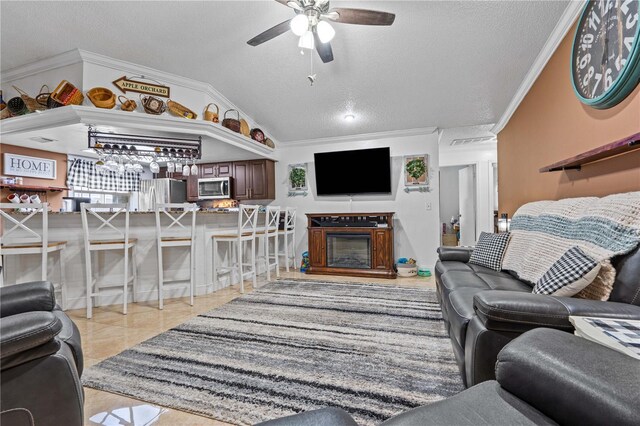 living room featuring crown molding, a textured ceiling, a ceiling fan, a glass covered fireplace, and vaulted ceiling