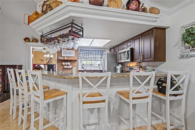 kitchen featuring appliances with stainless steel finishes, crown molding, dark brown cabinets, a breakfast bar, and light stone counters