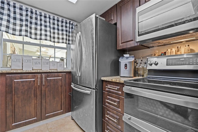kitchen featuring stainless steel appliances, light tile patterned floors, dark brown cabinets, and light stone counters