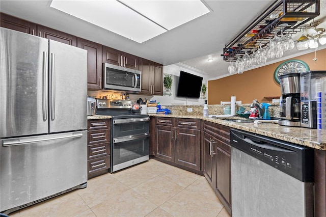 kitchen featuring appliances with stainless steel finishes, light tile patterned flooring, a sink, dark brown cabinetry, and light stone countertops