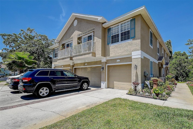 view of property featuring an attached garage, stucco siding, driveway, and a balcony