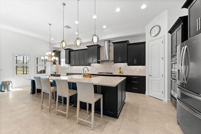 1416 Via Verdi Dr, Palm Harbor, FL 34683 - kitchen featuring stainless steel refrigerator with ice dispenser, wall chimney exhaust hood, dark cabinetry, a kitchen island with sink, and tasteful backsplash