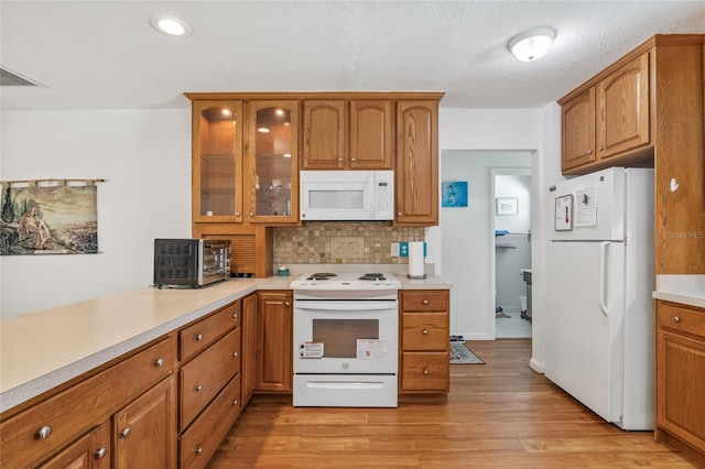 603 Royal Crest Dr, Brandon, FL 33511 - kitchen featuring white appliances, brown cabinetry, tasteful backsplash, light wood-style floors, and glass insert cabinets
