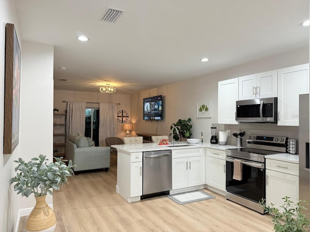 17099 Carleen Ave, Port Charlotte, FL 33948 - kitchen featuring appliances with stainless steel finishes, a peninsula, open floor plan, white cabinets, and light wood-style flooring