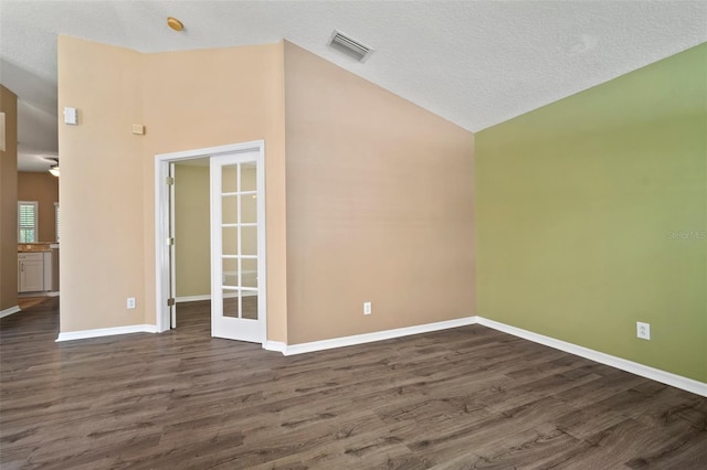 empty room featuring lofted ceiling, dark wood finished floors, baseboards, and a textured ceiling