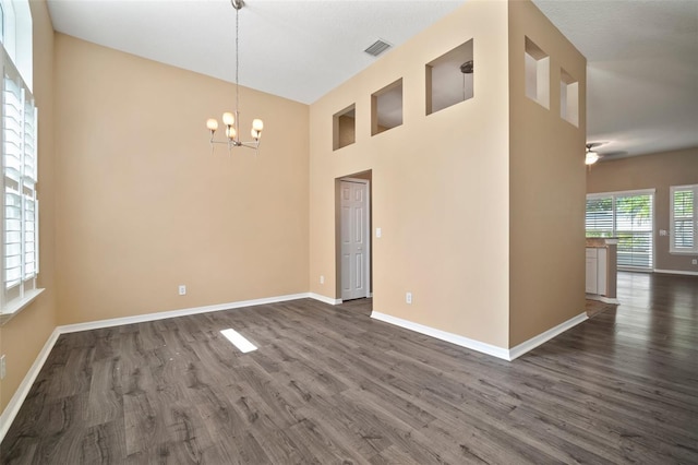 empty room featuring dark wood-style flooring, a chandelier, baseboards, ceiling fan, and a high ceiling