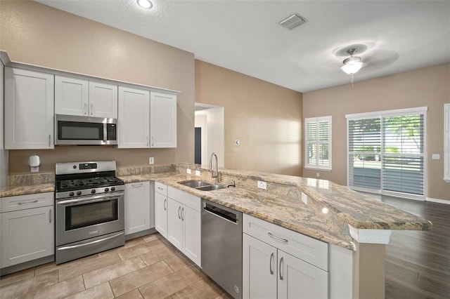 kitchen featuring stainless steel appliances, a sink, a peninsula, ceiling fan, and light stone countertops