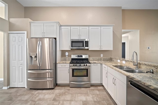 kitchen with appliances with stainless steel finishes, a sink, light stone counters, and white cabinets