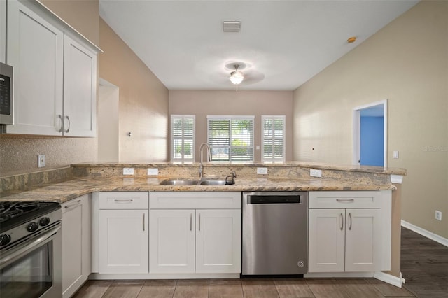 kitchen featuring appliances with stainless steel finishes, a sink, white cabinets, light stone counters, and a peninsula