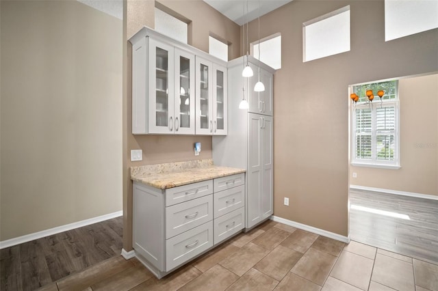 kitchen featuring baseboards, glass insert cabinets, hanging light fixtures, and white cabinets