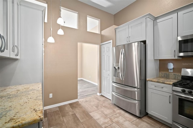 kitchen featuring appliances with stainless steel finishes, pendant lighting, light stone countertops, gray cabinetry, and baseboards