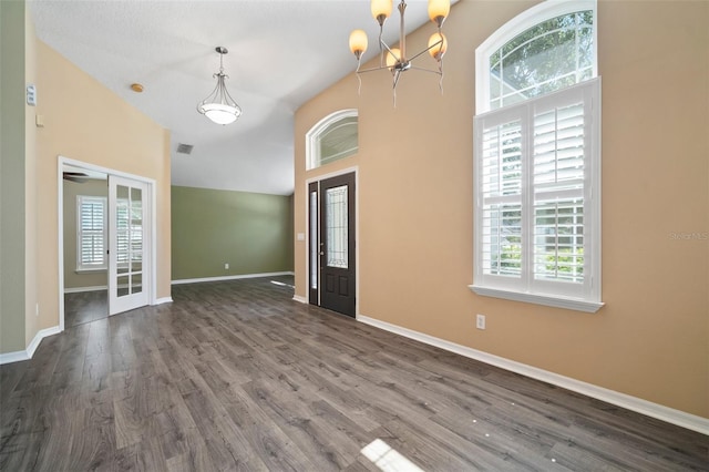 unfurnished living room featuring a chandelier, a high ceiling, dark wood finished floors, baseboards, and french doors