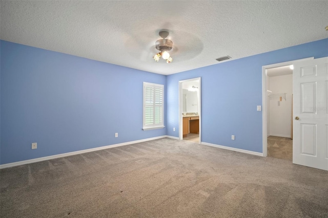 unfurnished bedroom featuring carpet, a textured ceiling, baseboards, ceiling fan, and ensuite bath