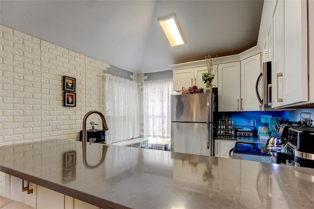 2721 Baird Ct, Palm Harbor, FL 34684 - kitchen with stainless steel appliances, stainless steel counters, a peninsula, white cabinets, and vaulted ceiling