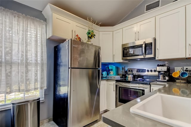2721 Baird Ct, Palm Harbor, FL 34684 - kitchen featuring appliances with stainless steel finishes, vaulted ceiling, white cabinetry, a sink, and light tile patterned floors