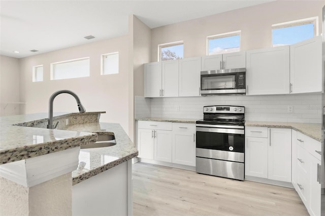 3023 Minuteman Ln, Brandon, FL 33511 - kitchen with appliances with stainless steel finishes, a sink, light wood-style floors, backsplash, and white cabinets