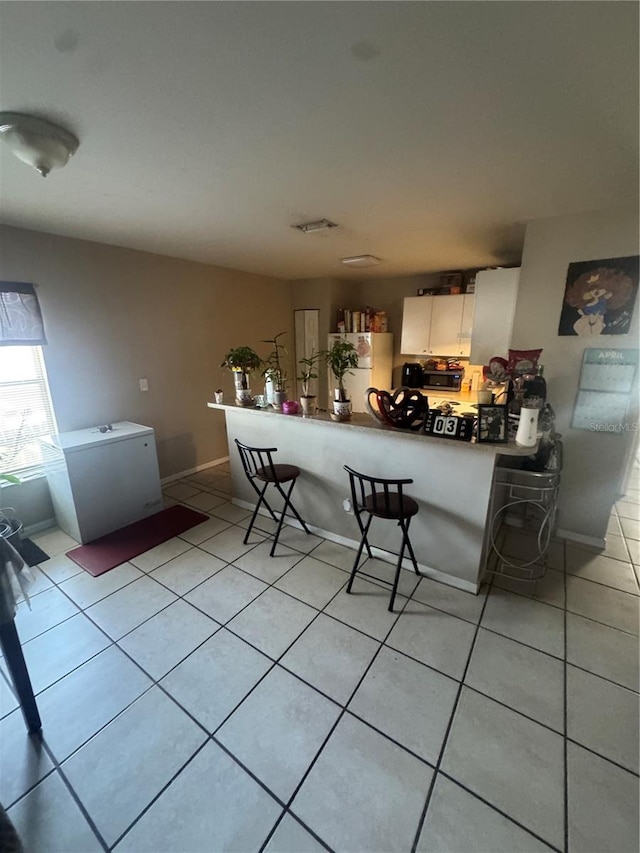 3710 N 57th St, Tampa, FL 33619 - kitchen featuring freestanding refrigerator, light tile patterned floors, a breakfast bar area, a peninsula, and white cabinetry