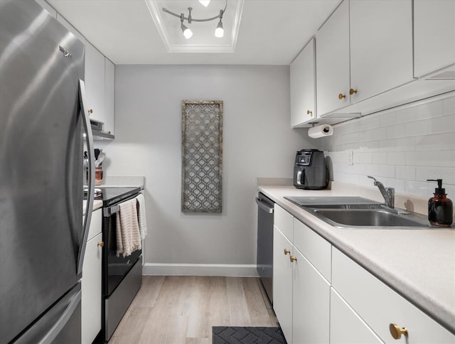 kitchen with appliances with stainless steel finishes, a sink, light wood-style floors, tasteful backsplash, and light countertops