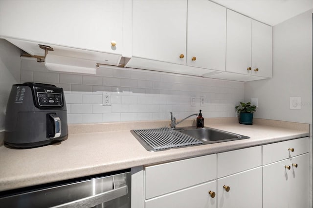 kitchen featuring a sink, stainless steel dishwasher, white cabinets, light countertops, and backsplash