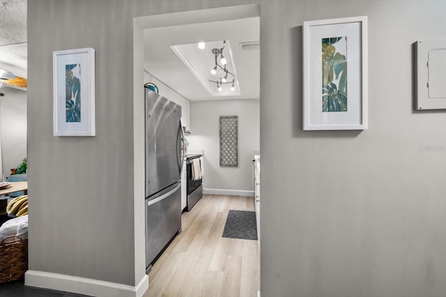 kitchen with freestanding refrigerator, a raised ceiling, light wood finished floors, electric panel, and baseboards