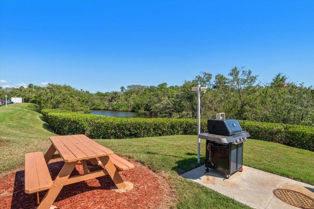 view of grassy yard featuring a water view, a wooded view, and a patio area