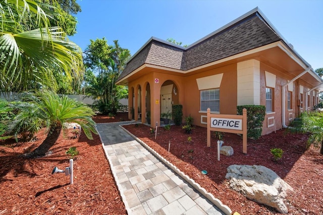 view of front of property featuring a shingled roof, mansard roof, and stucco siding