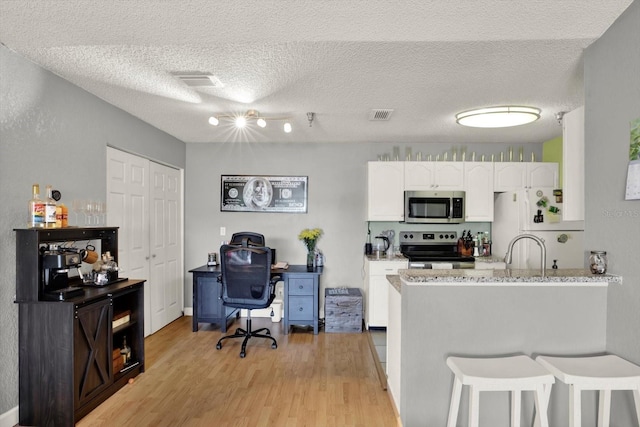 10265 Gandy Blvd N Unit 906, Saint Petersburg, FL 33702 - kitchen featuring stainless steel appliances, white cabinets, light wood-style floors, a peninsula, and a kitchen bar