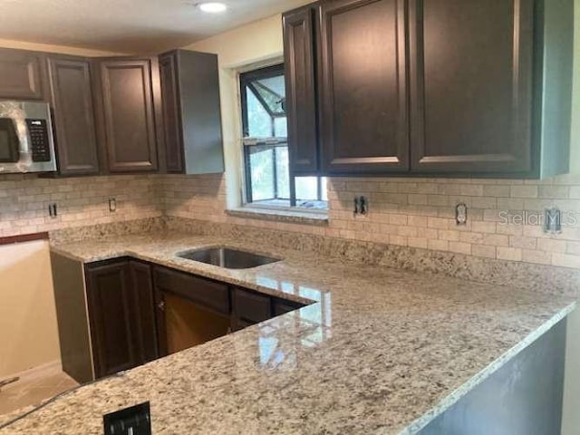 17220 Estes Rd, Lutz, FL 33548 - kitchen with stainless steel microwave, light stone countertops, tasteful backsplash, and dark brown cabinetry