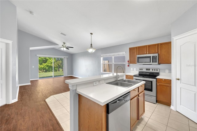 kitchen with appliances with stainless steel finishes, a sink, vaulted ceiling, brown cabinets, and open floor plan