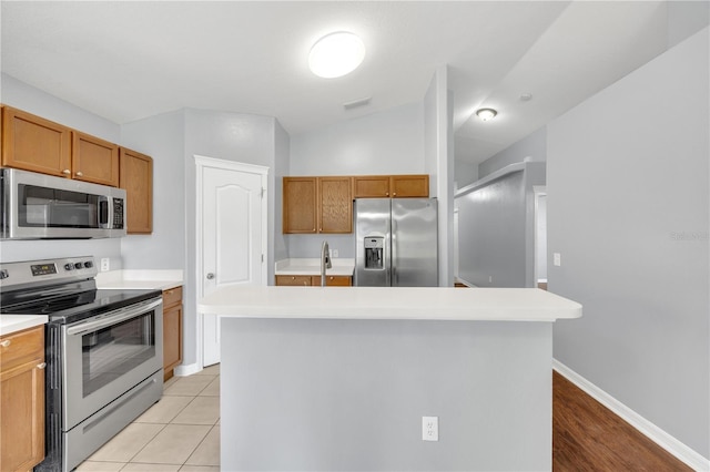 kitchen with appliances with stainless steel finishes, light countertops, brown cabinetry, lofted ceiling, and a kitchen island