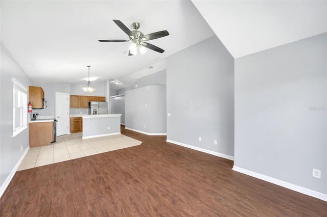 unfurnished living room with vaulted ceiling, a ceiling fan, baseboards, and light wood-style floors