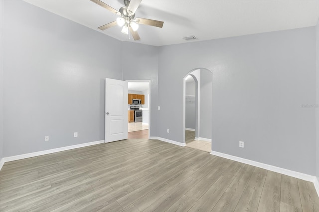 unfurnished bedroom featuring arched walkways, light wood finished floors, baseboards, a spacious closet, and ceiling fan