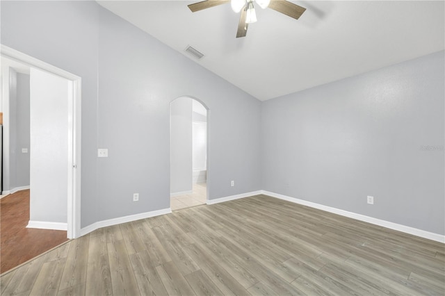 empty room with arched walkways, lofted ceiling, ceiling fan, light wood-type flooring, and baseboards